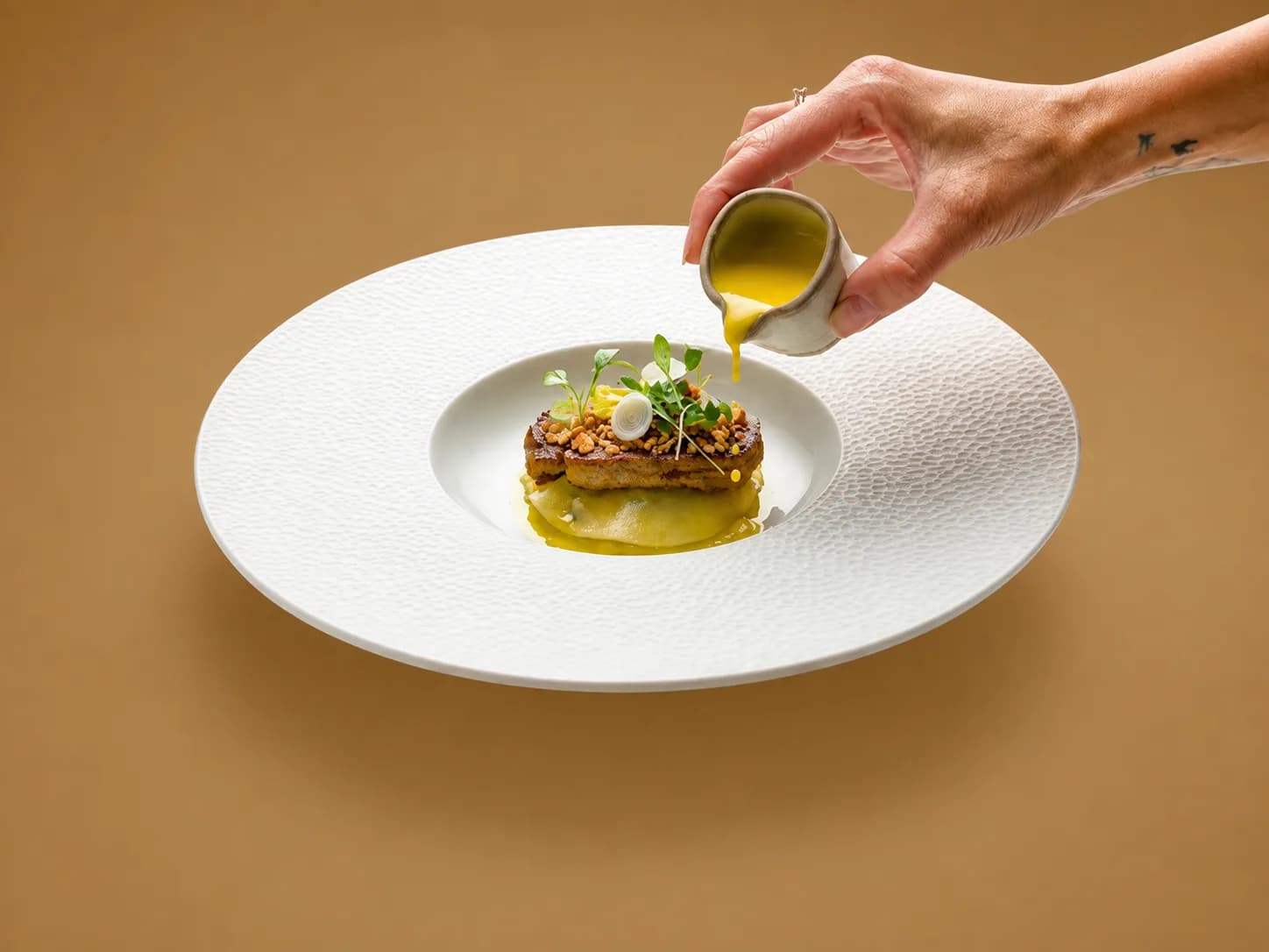 Sauce verte versée à la main autour d'une bouchée garnie de jeunes pousses