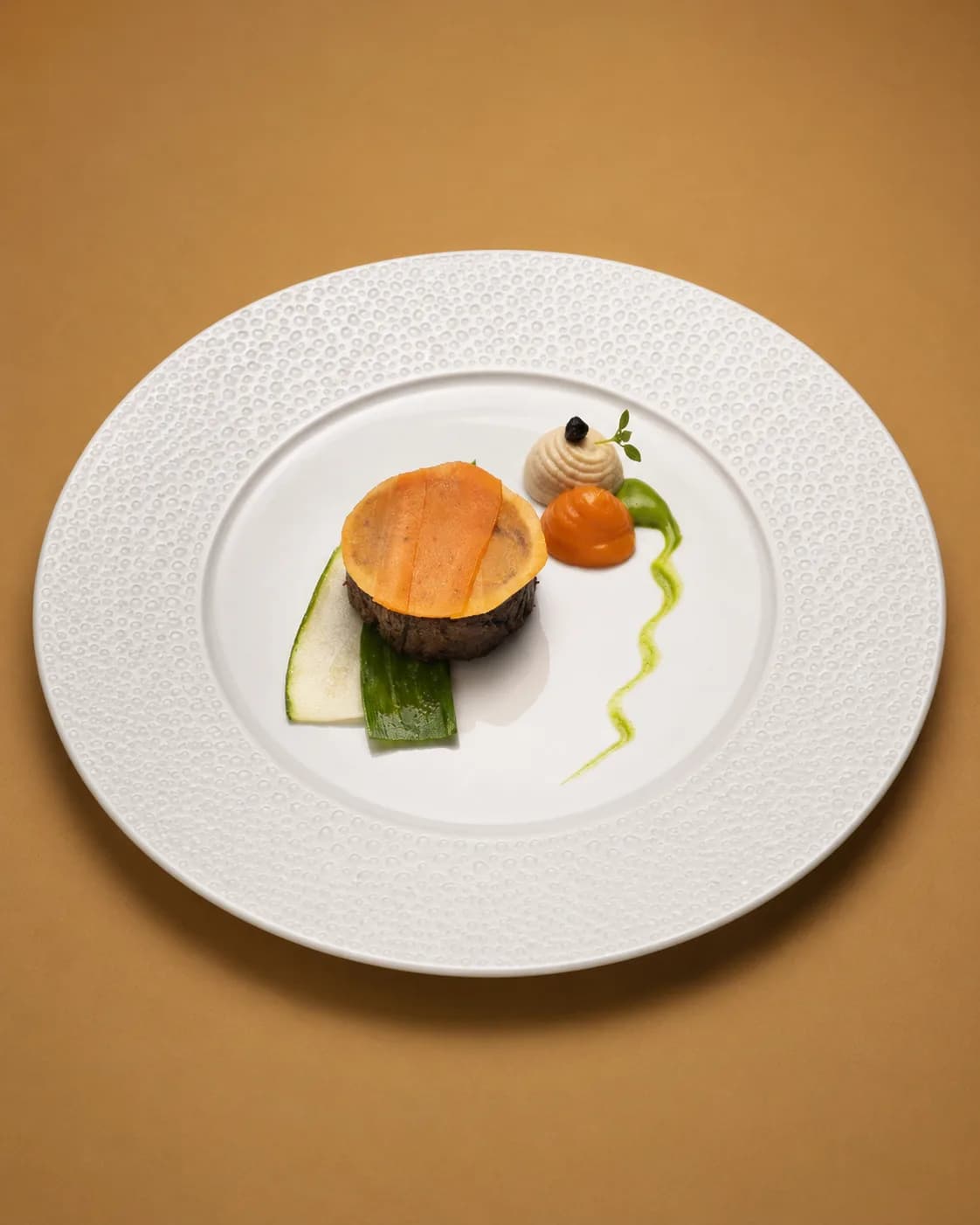 Pièce de bœuf coiffée d'un disque de carotte, courgette et deux quenelles de purée sur une assiette à marli perlé