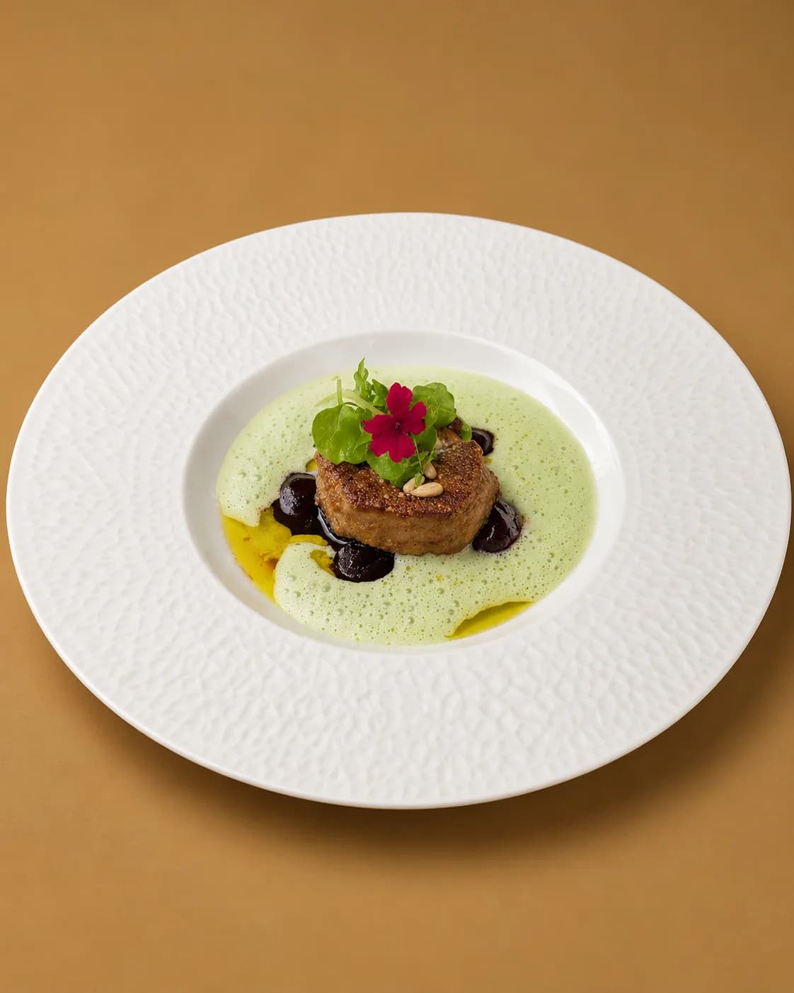 Foie gras poêlé cerné de cerises et de pignons dans une écume verte, fleur rose posée dessus
