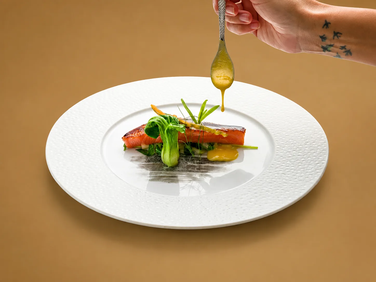 Poisson et légumes verts nappés à la cuillère dans une assiette blanche